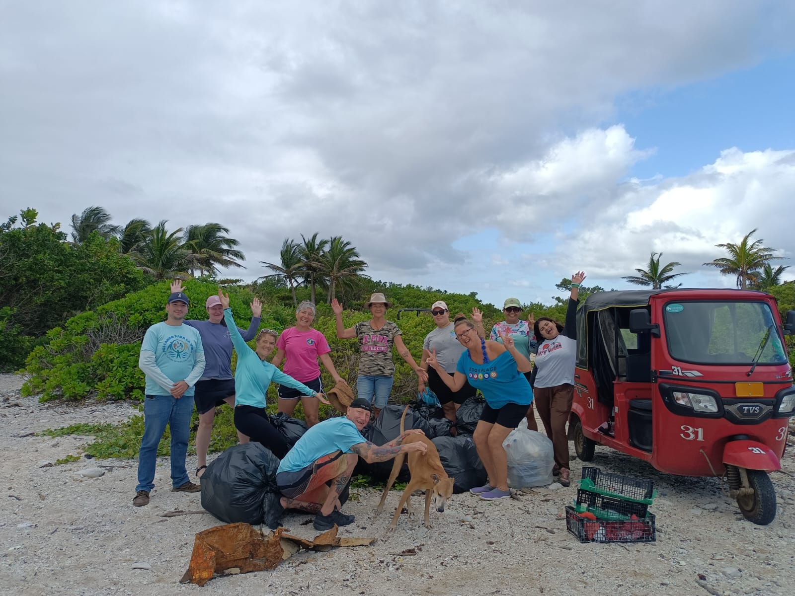 Cleanup volunteers pose with a red TukTuk and dog on Tradewinds Beach on February 25th 2026.