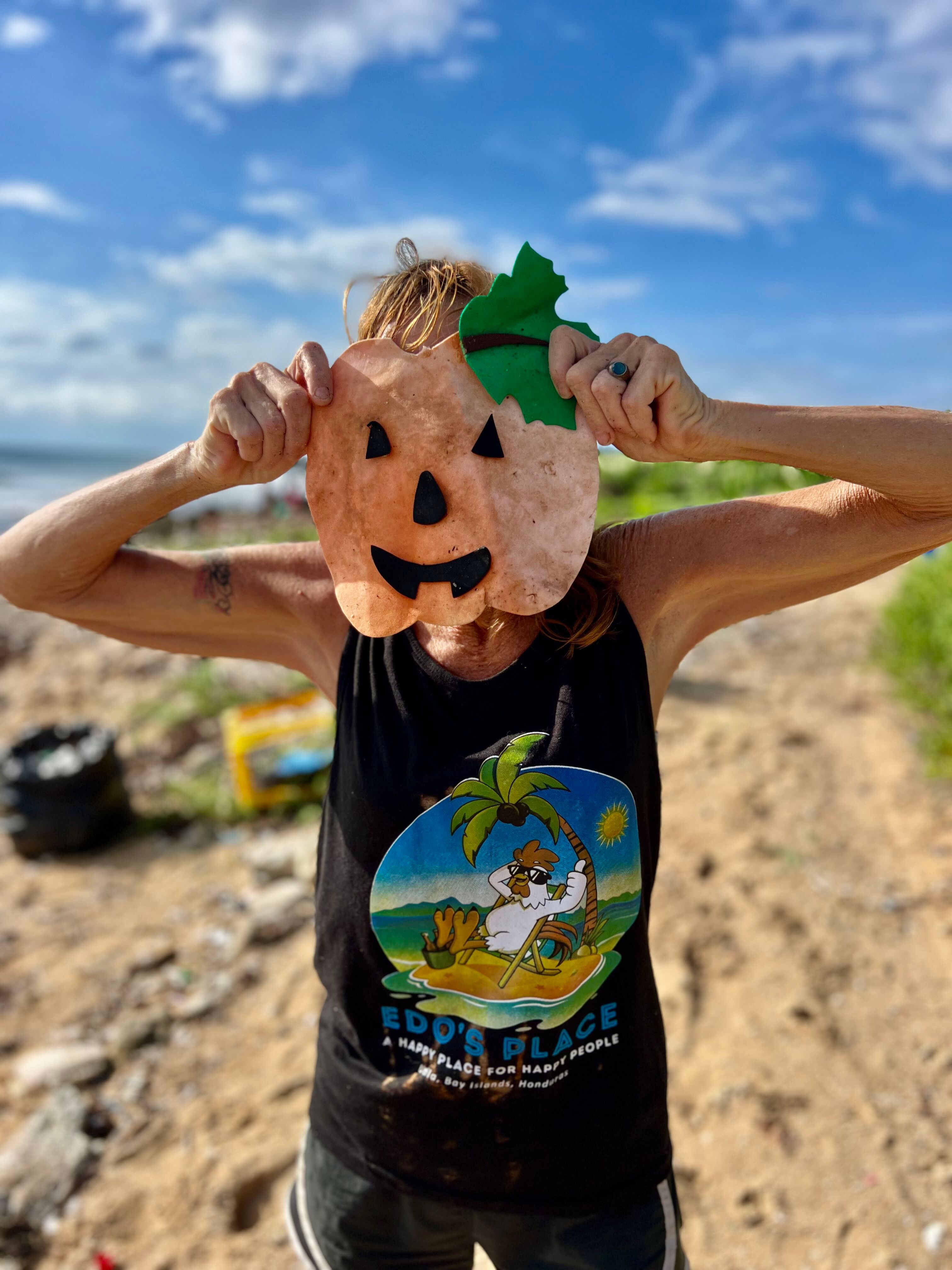 A volunteer holding up a large, handmade cardboard Jack-o'-lantern face found during a cleanup.